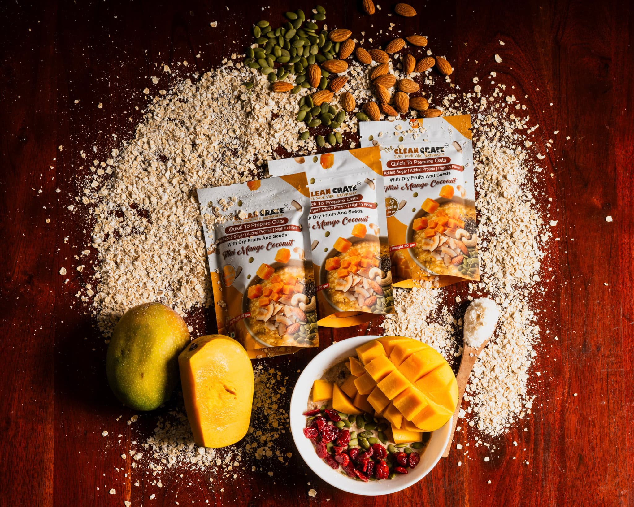 Thai Mango Coconut packs surrounded by rolled oats, almonds and pumpkin seeds, with a bowl of prepared oats and fresh mango