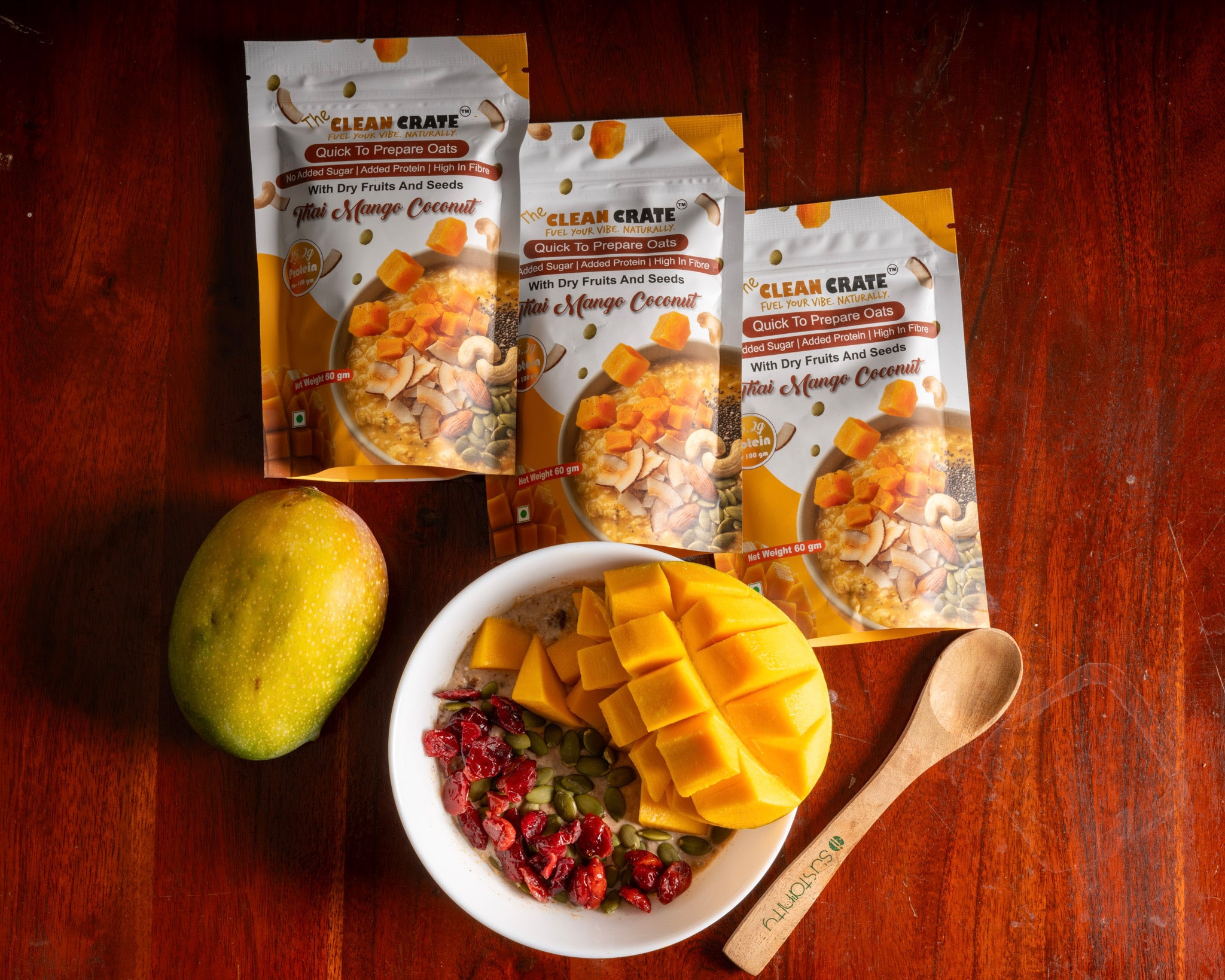 Thai Mango Coconut protein oat packs beside a bowl of oats topped with fresh mango, cranberries and pumpkin seeds